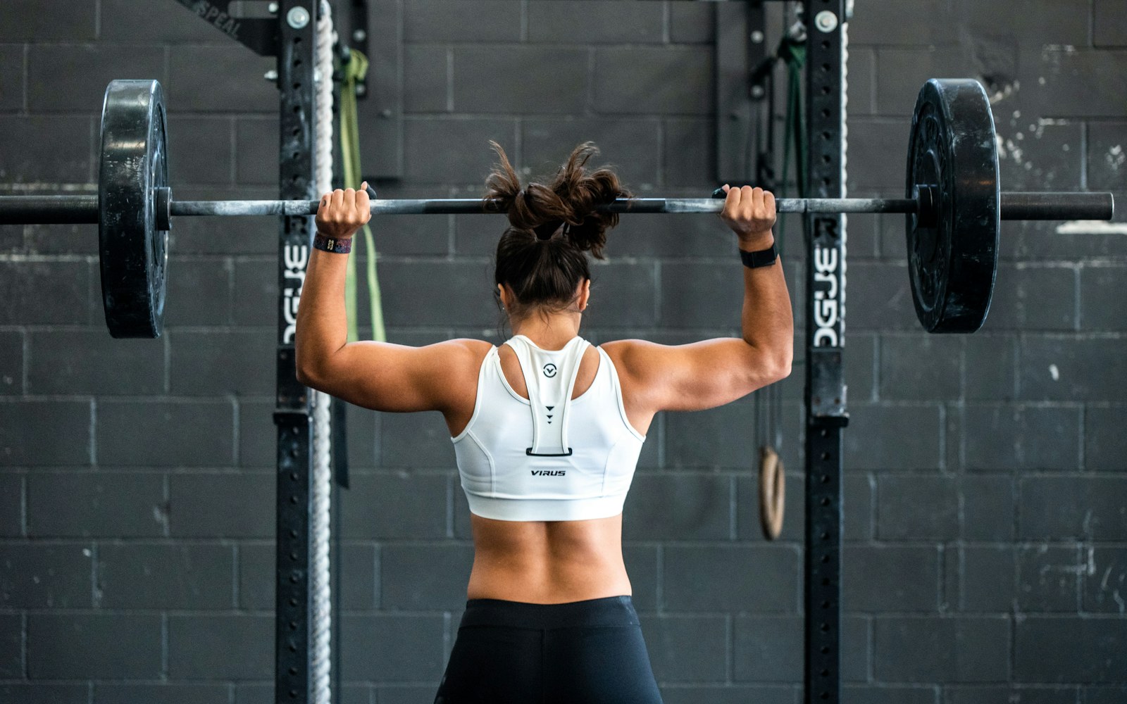 Woman presses a loaded barbell overhead in a strength-training gym