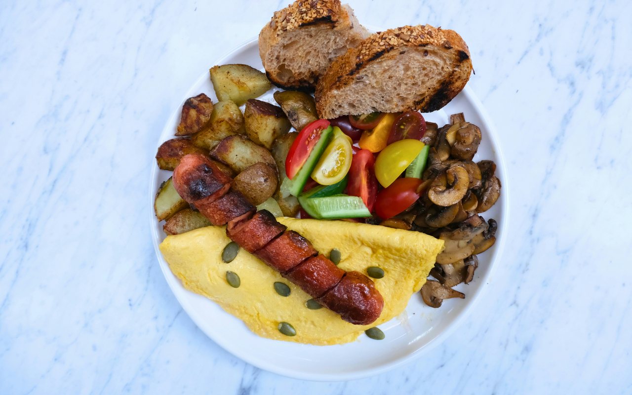 Breakfast plate with sliced sausage, eggs, potatoes, mushrooms, tomatoes, cucumbers, and bread.