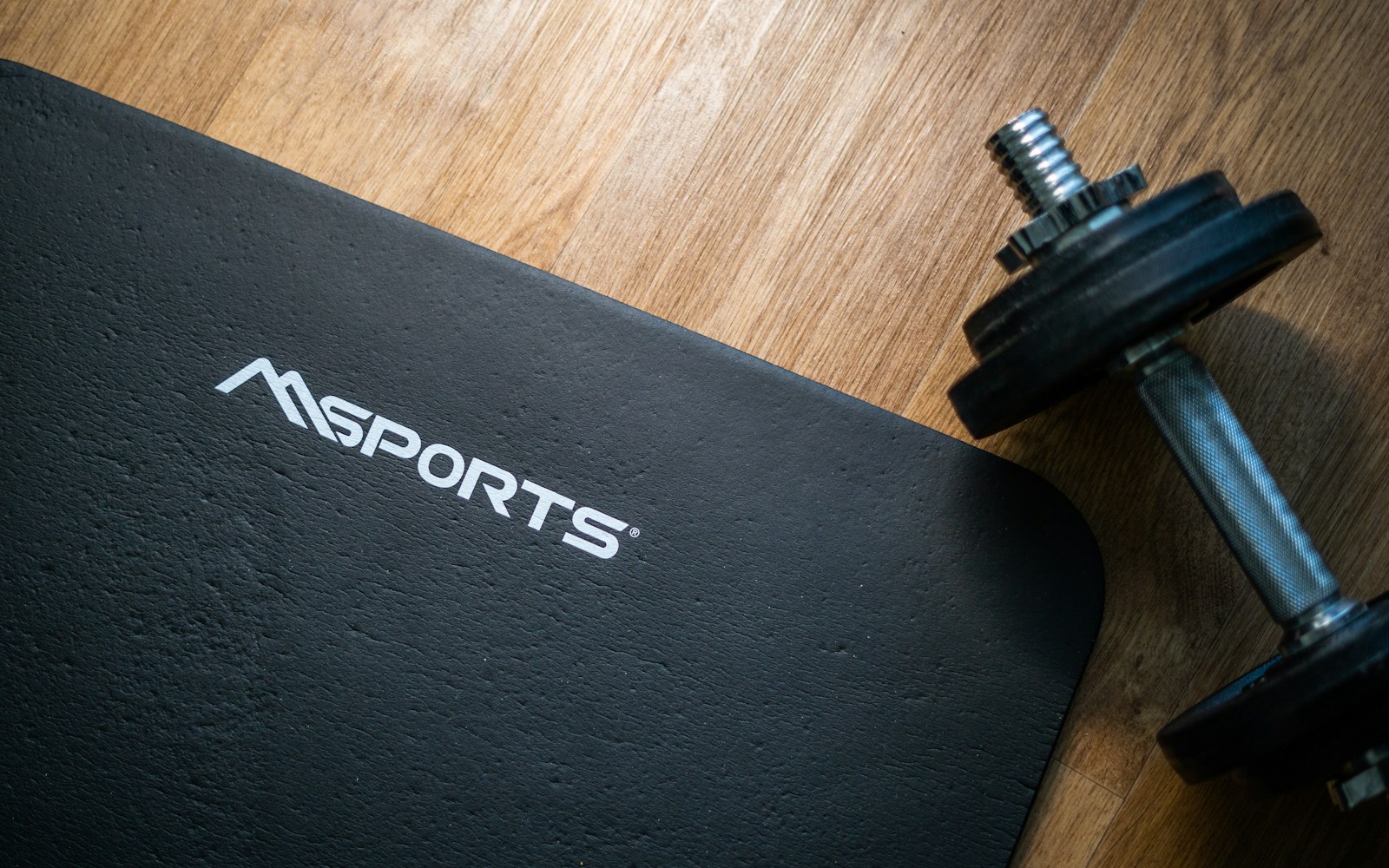 Exercise mat and adjustable dumbbell on a wooden floor