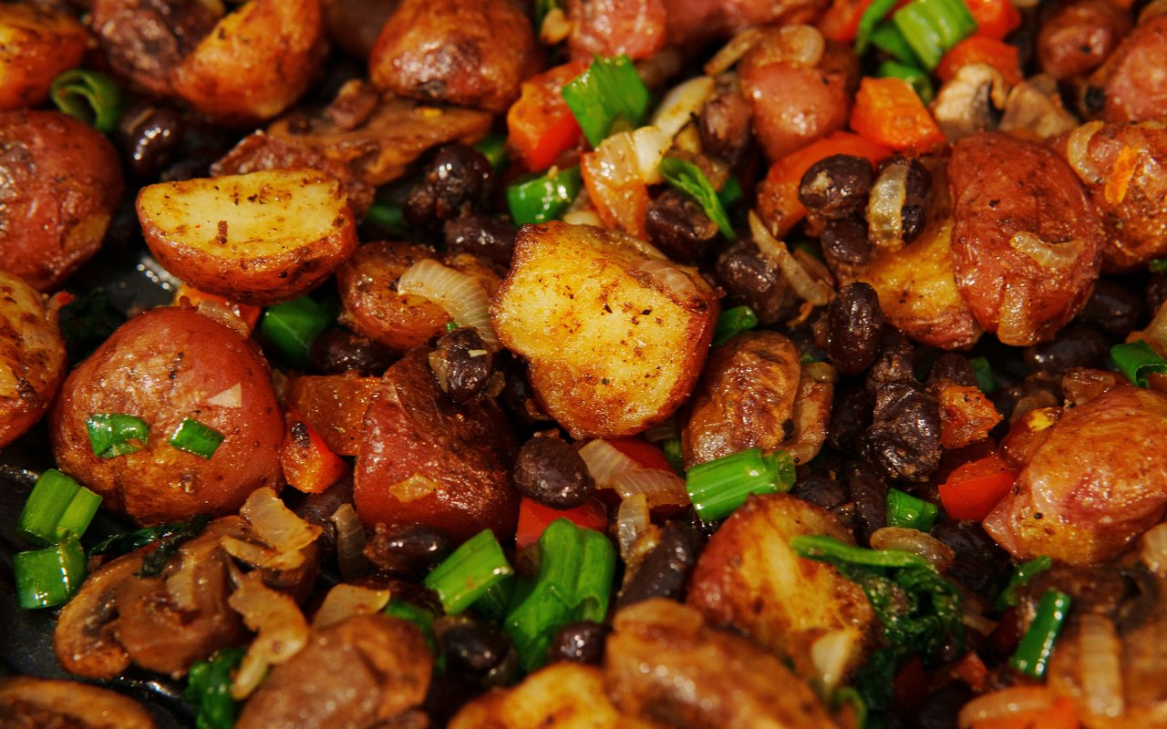 Close-up of roasted red potatoes with black beans, mushrooms, bell peppers, onions, and scallions.