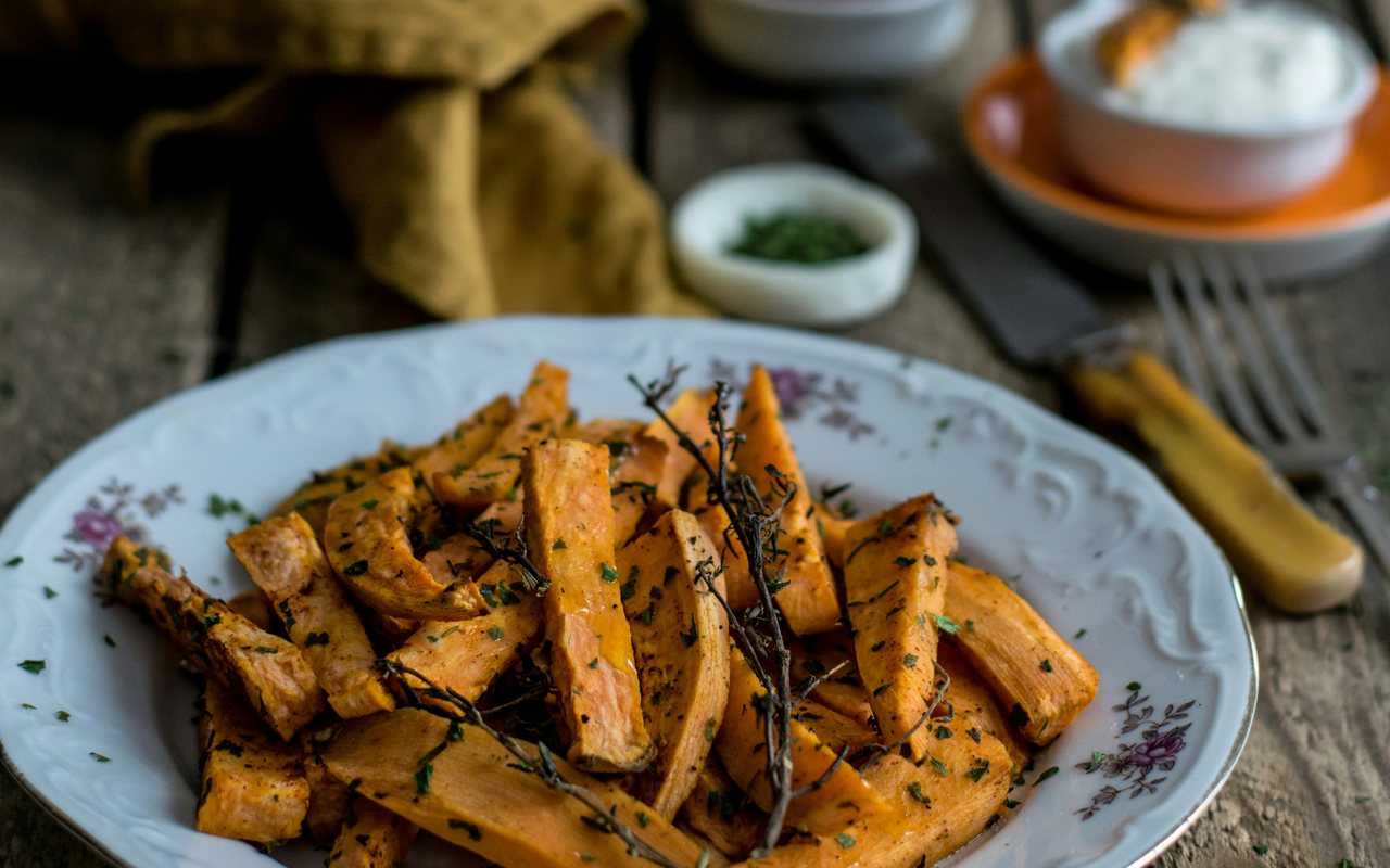 Baked sweet potato wedges seasoned with chopped herbs and whole herb sprigs.