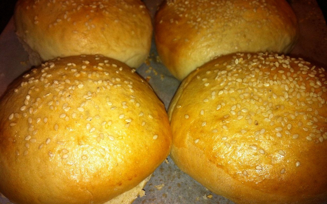Four round golden sandwich rolls, two topped with sesame seeds