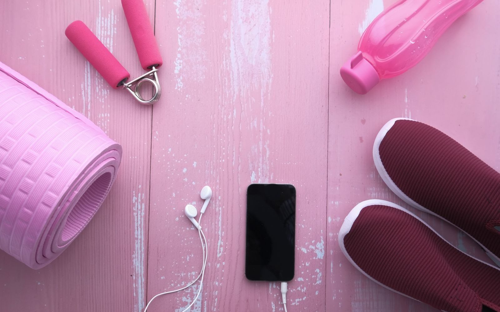 Workout shoes, exercise mat, water bottle, phone, and earphones laid out together.