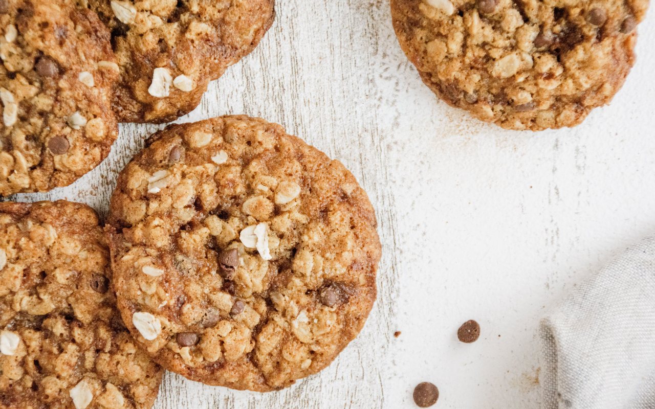 Golden oatmeal cookies with visible rolled oats and chocolate chips on a white wooden surface