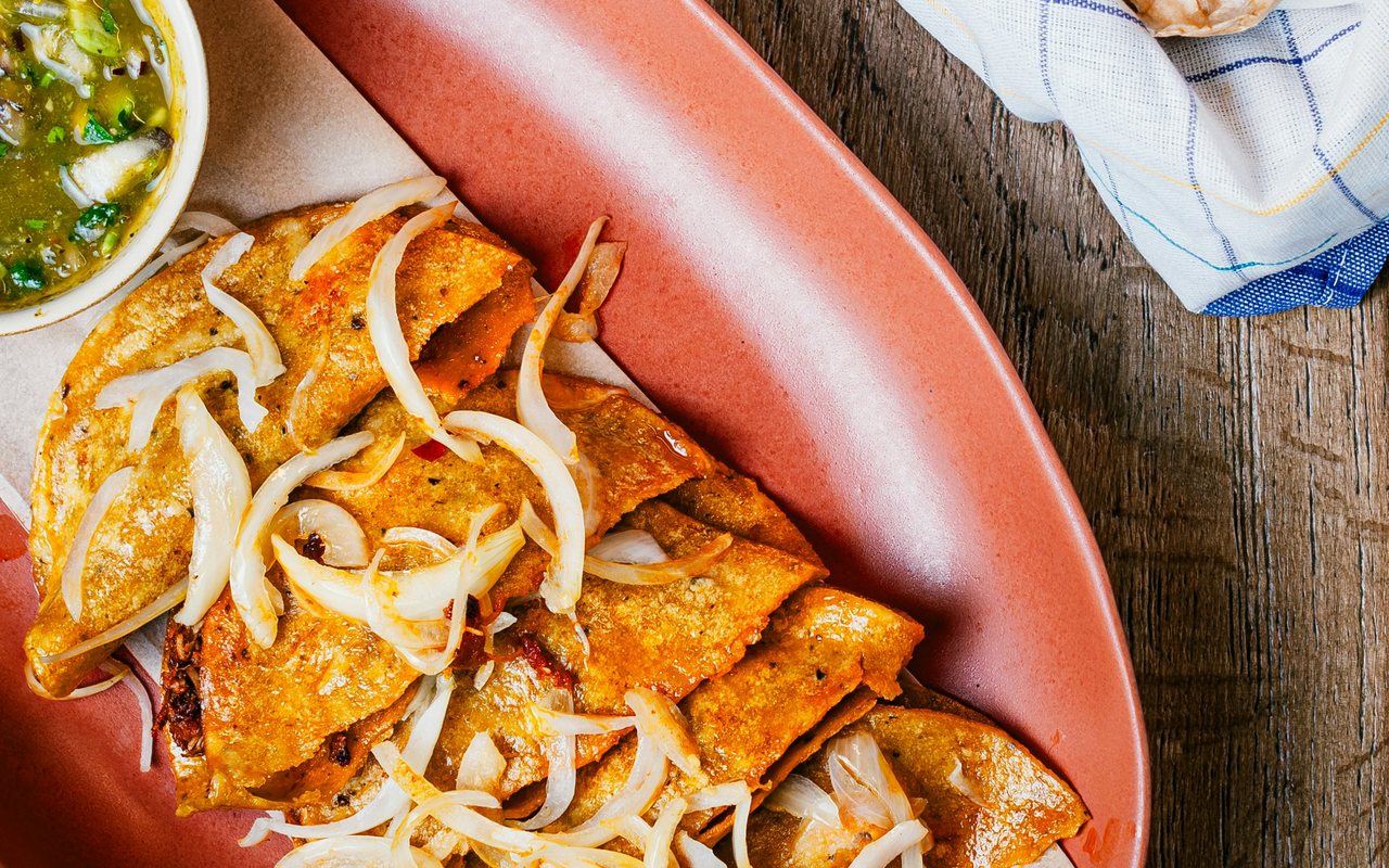 Red-sauced enchiladas topped with sliced onions in a parchment-lined serving basket.