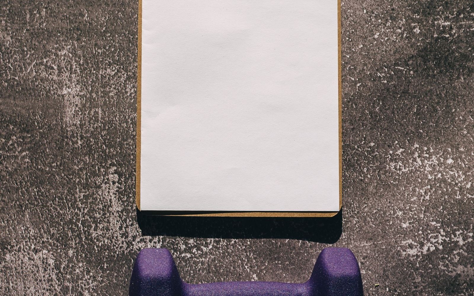 Blank clipboard and purple dumbbell on a textured gym floor.