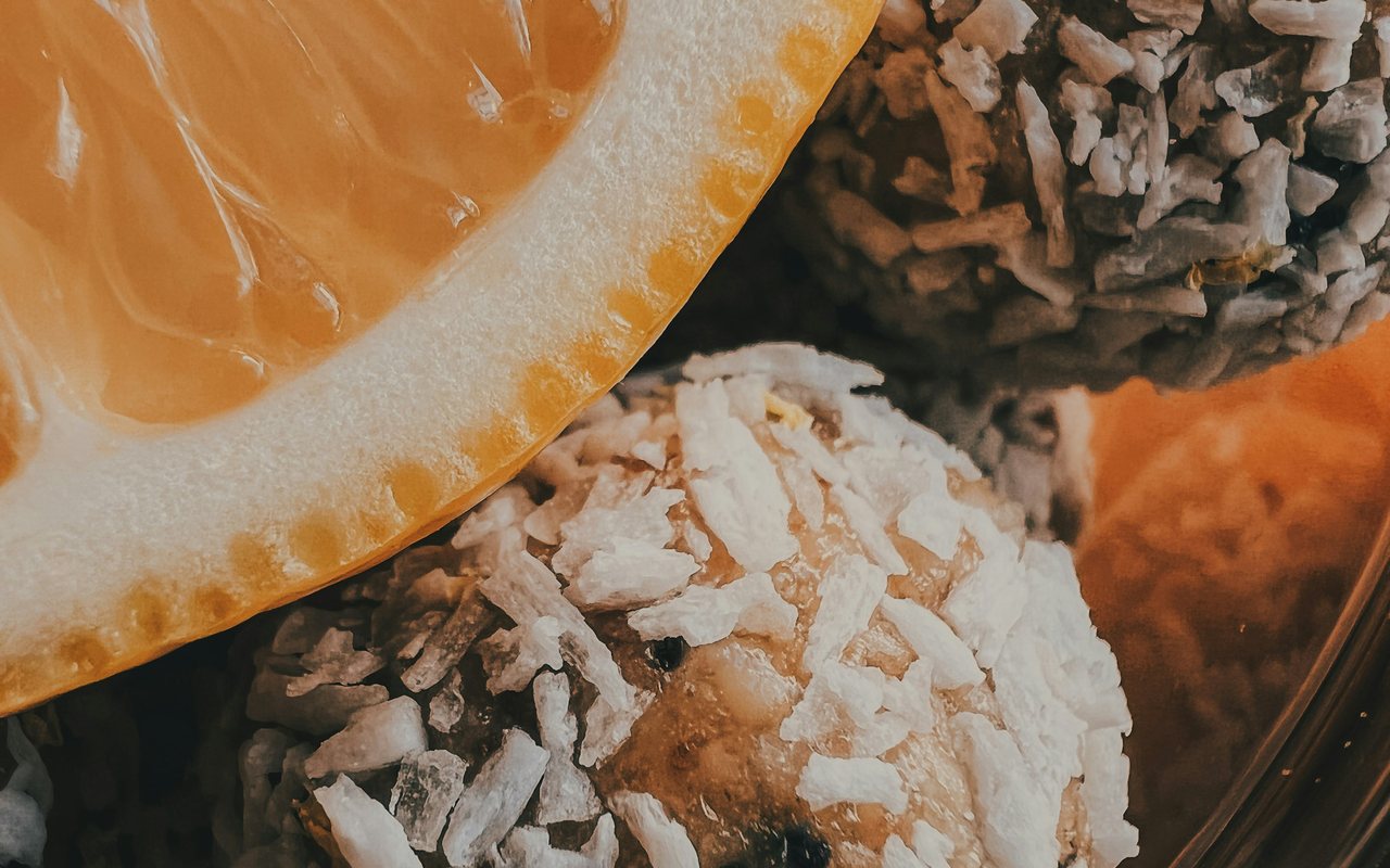 Coconut-coated energy bites beside a halved orange in a close-up view.