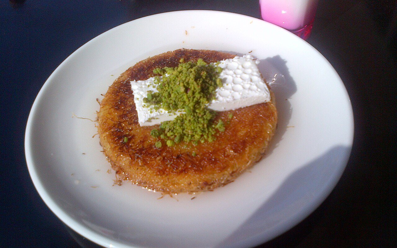 Round golden künefe with melted cheese inside and syrup spooned over the top