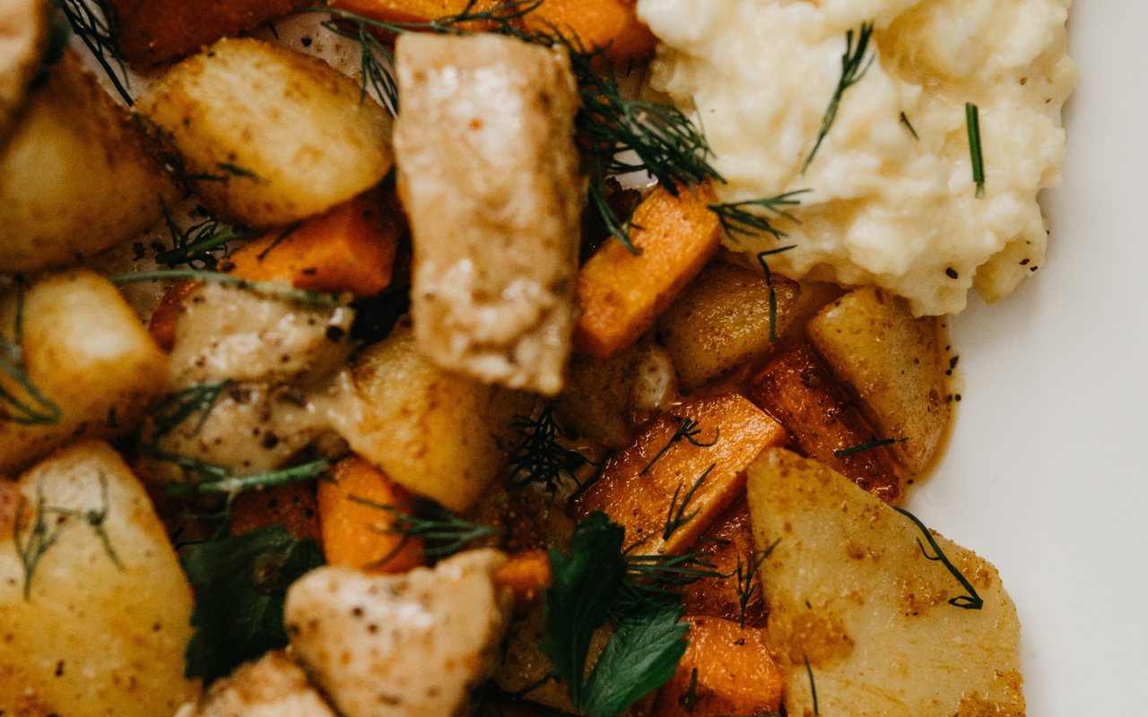 Sautéed chicken strips with browned potato rounds and carrots on a plate