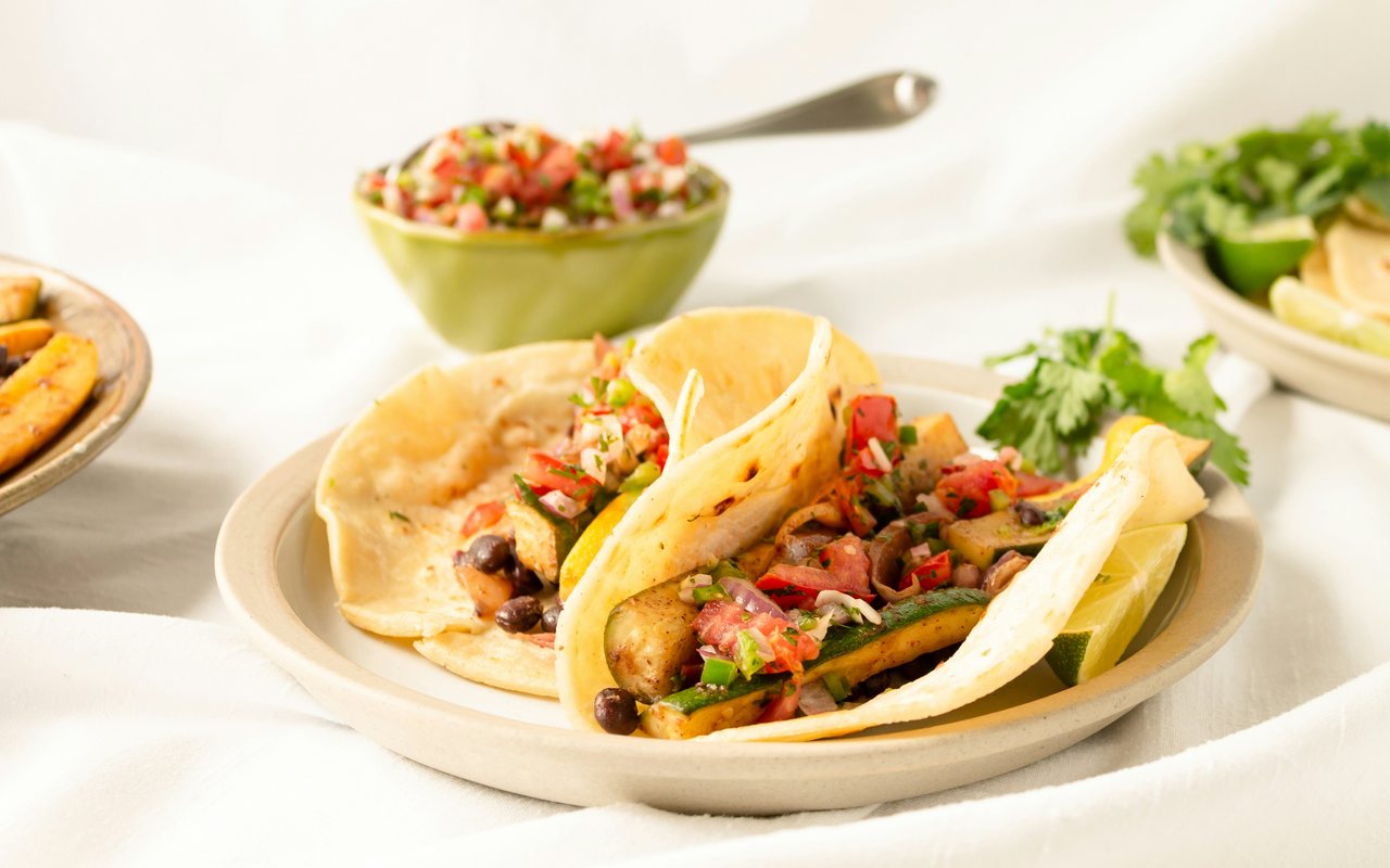 Corn-tortilla tacos with zucchini, black beans, tomato-onion salsa, herbs, and citrus.