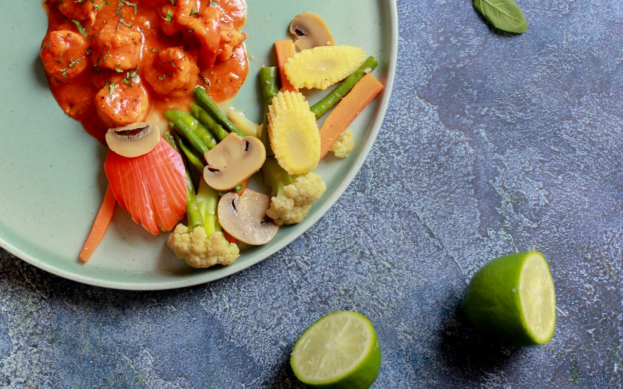 Shrimp in red sauce with mushrooms, tomatoes, peppers, greens, and halved limes.