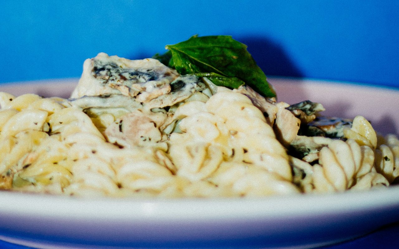 Creamy spiral pasta with spinach and mushrooms in a pale pink bowl against a blue background.