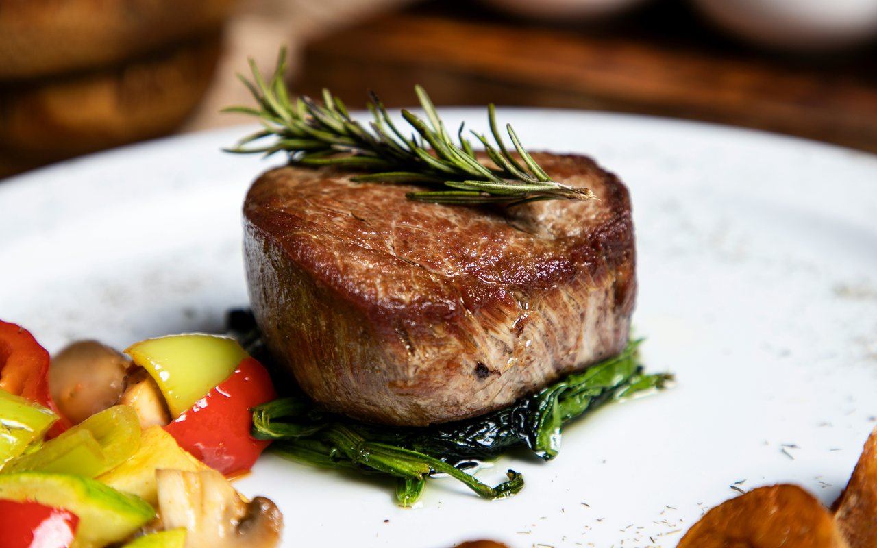 Sliced steak with roasted red and yellow peppers, mushrooms, greens, and rosemary.
