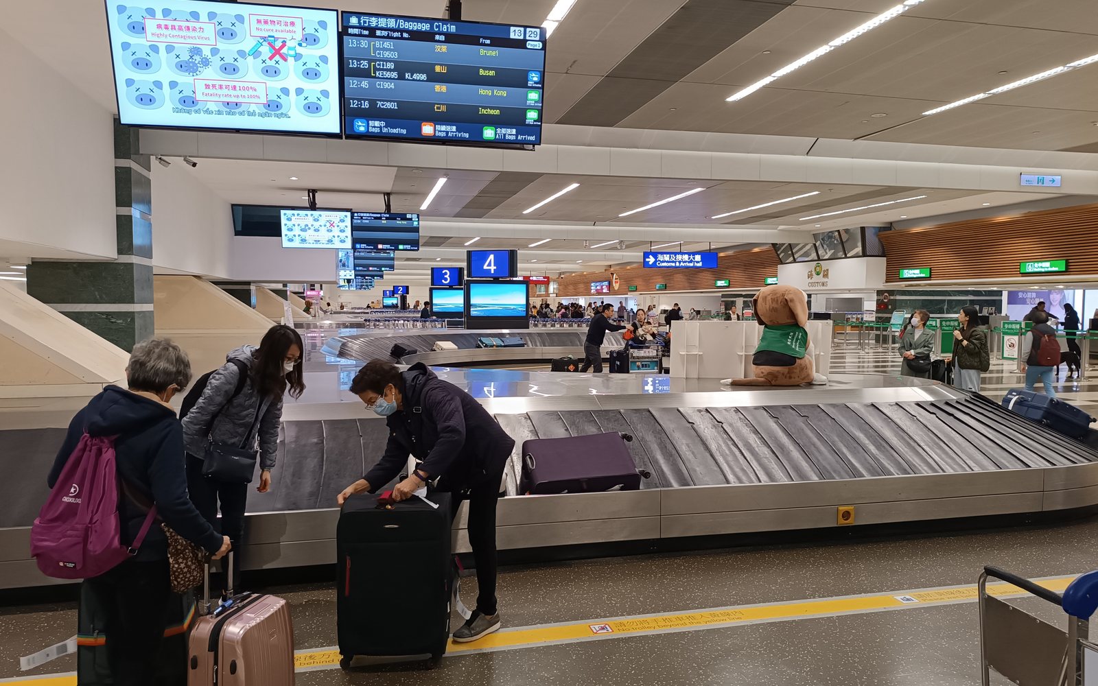Travelers collect suitcases from a busy airport baggage carousel.
