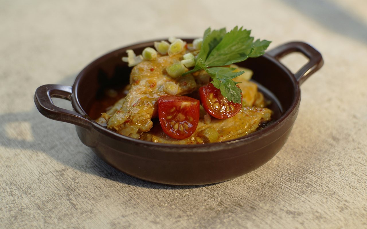 Stir-fried chicken topped with sliced tomatoes, scallions, and celery leaves in a brown serving dish.