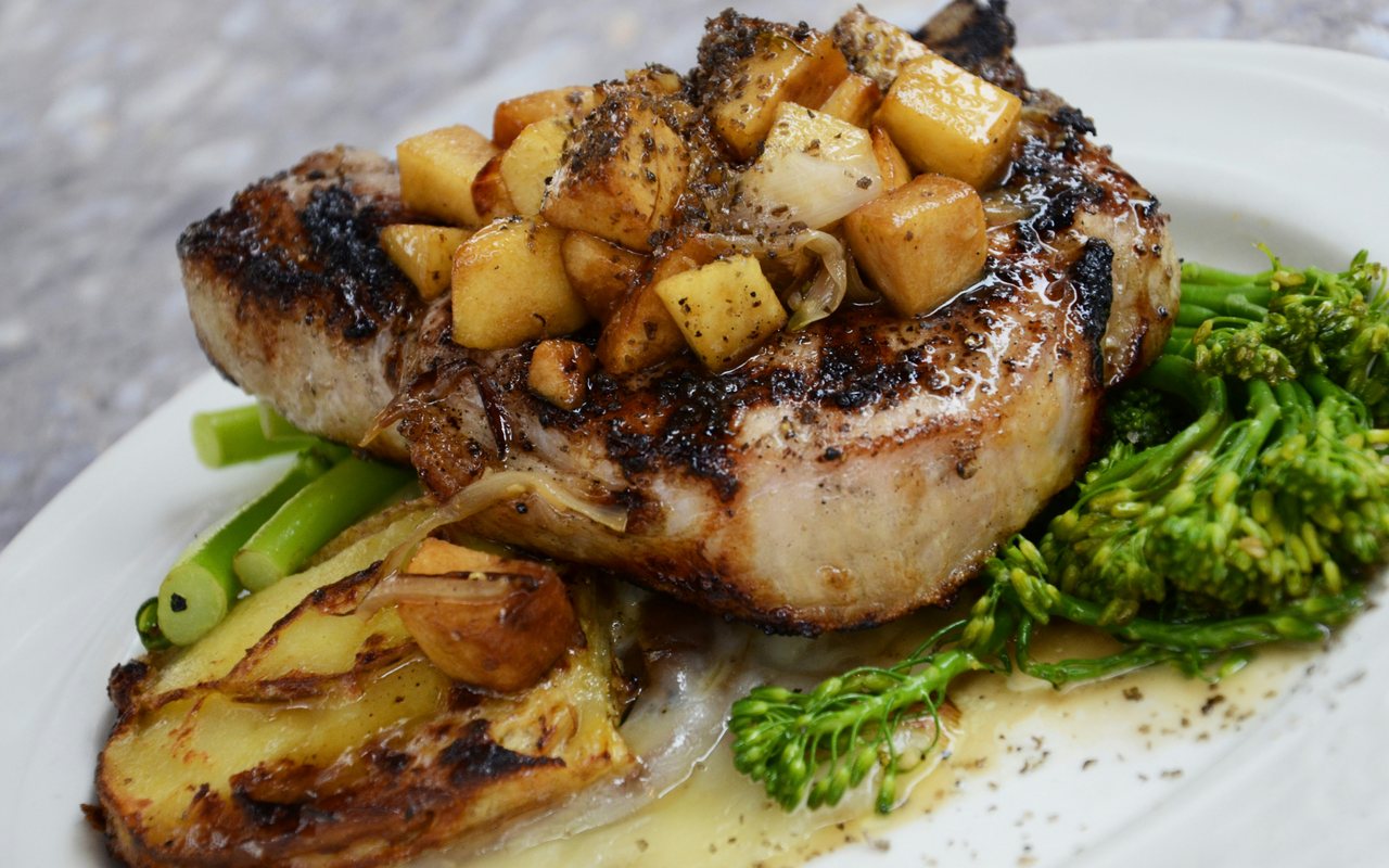 Cooked pork chop with roasted potatoes, onions, broccolini, and creamy sauce.