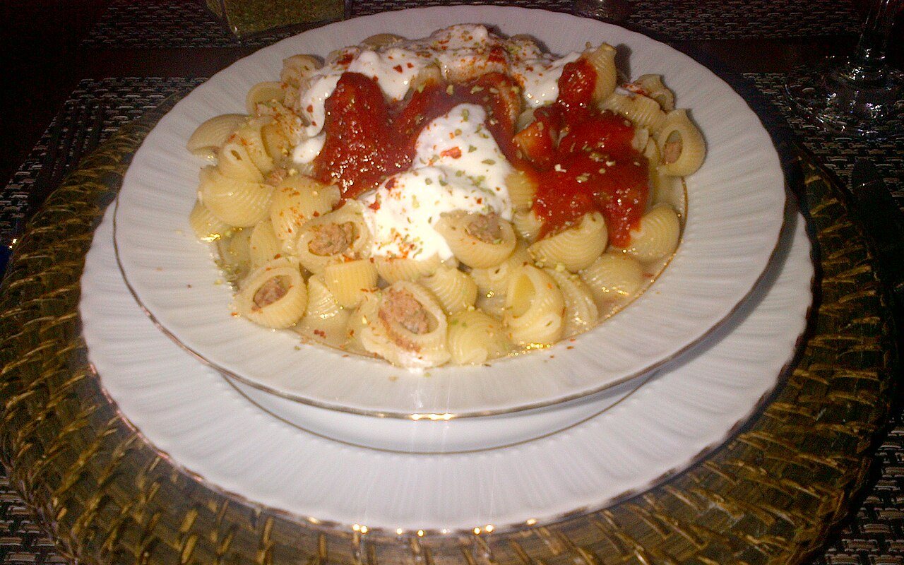 Yogurt-coated pasta topped with tomato-paste onions in a serving bowl