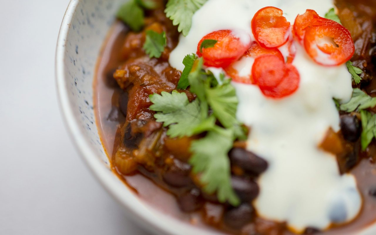 Bean chili topped with creamy white sauce, cilantro, sliced chiles, and scallions.