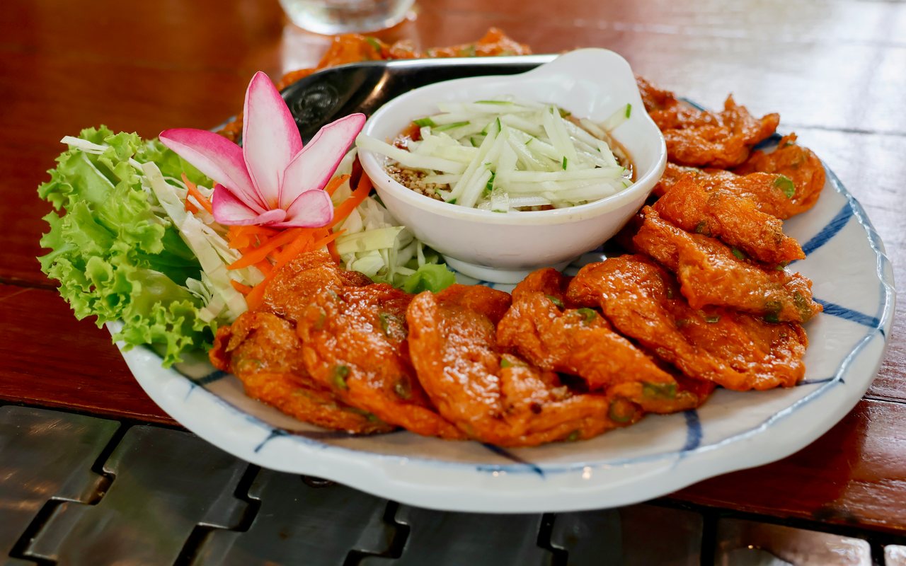 Browned fish cakes served with shredded cabbage and carrot slaw, cucumbers, and dipping sauce.