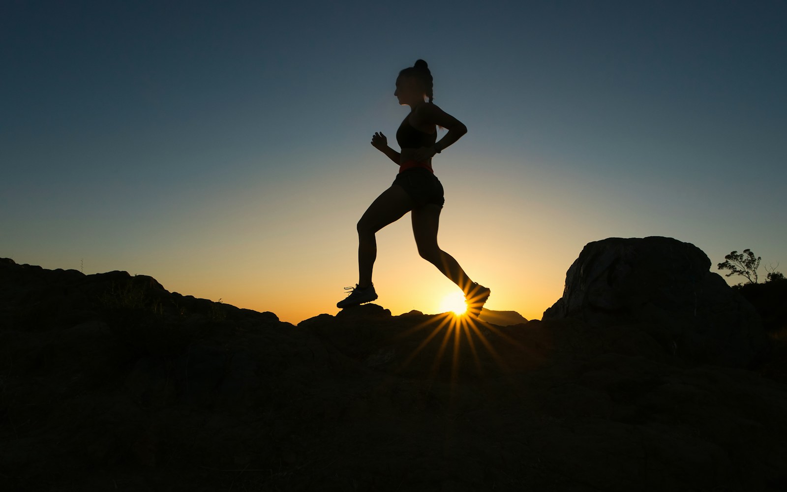 Runner silhouetted against a low sun on a rocky trail