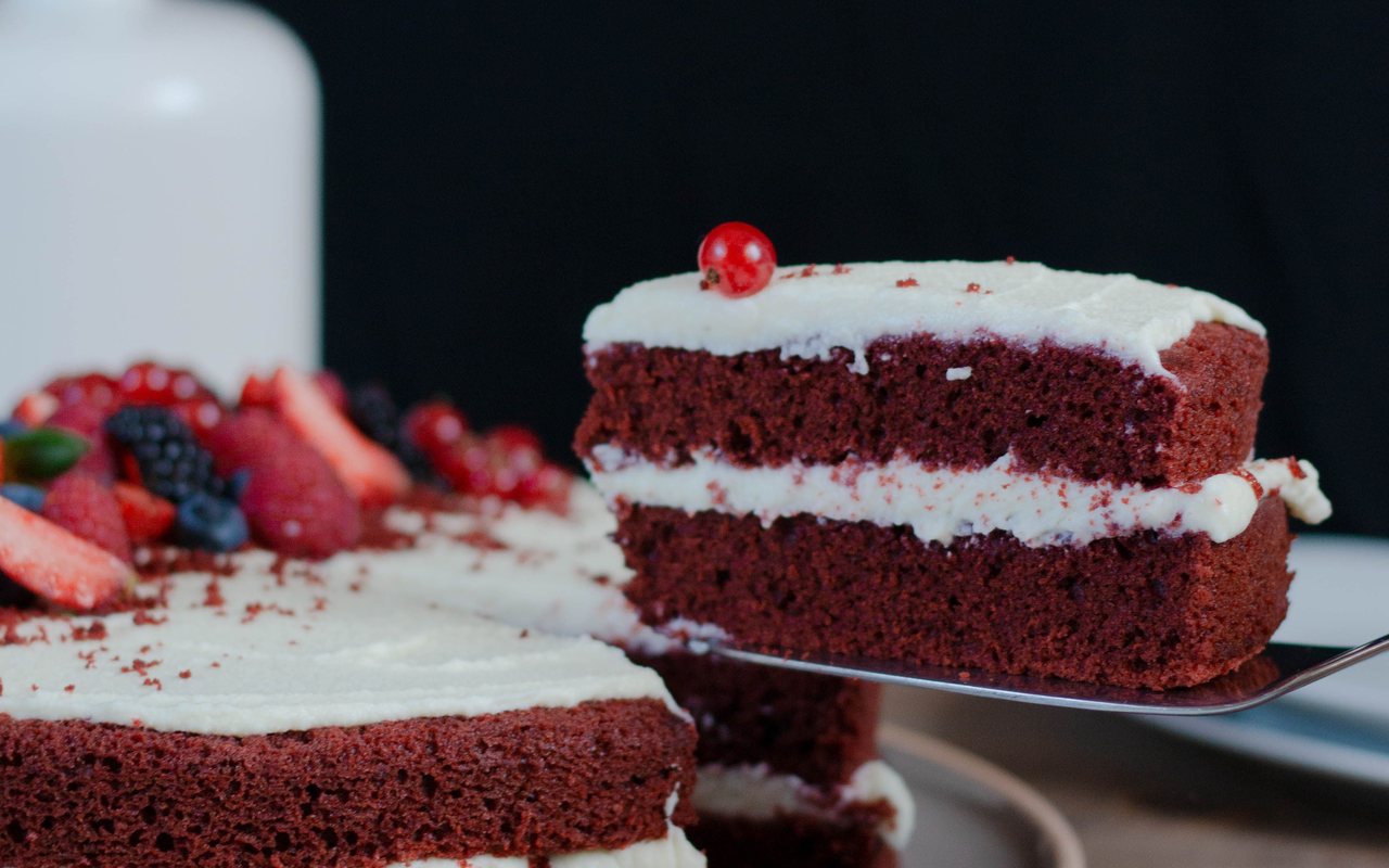 Two-layer red velvet cake covered with white frosting and red cake crumbs