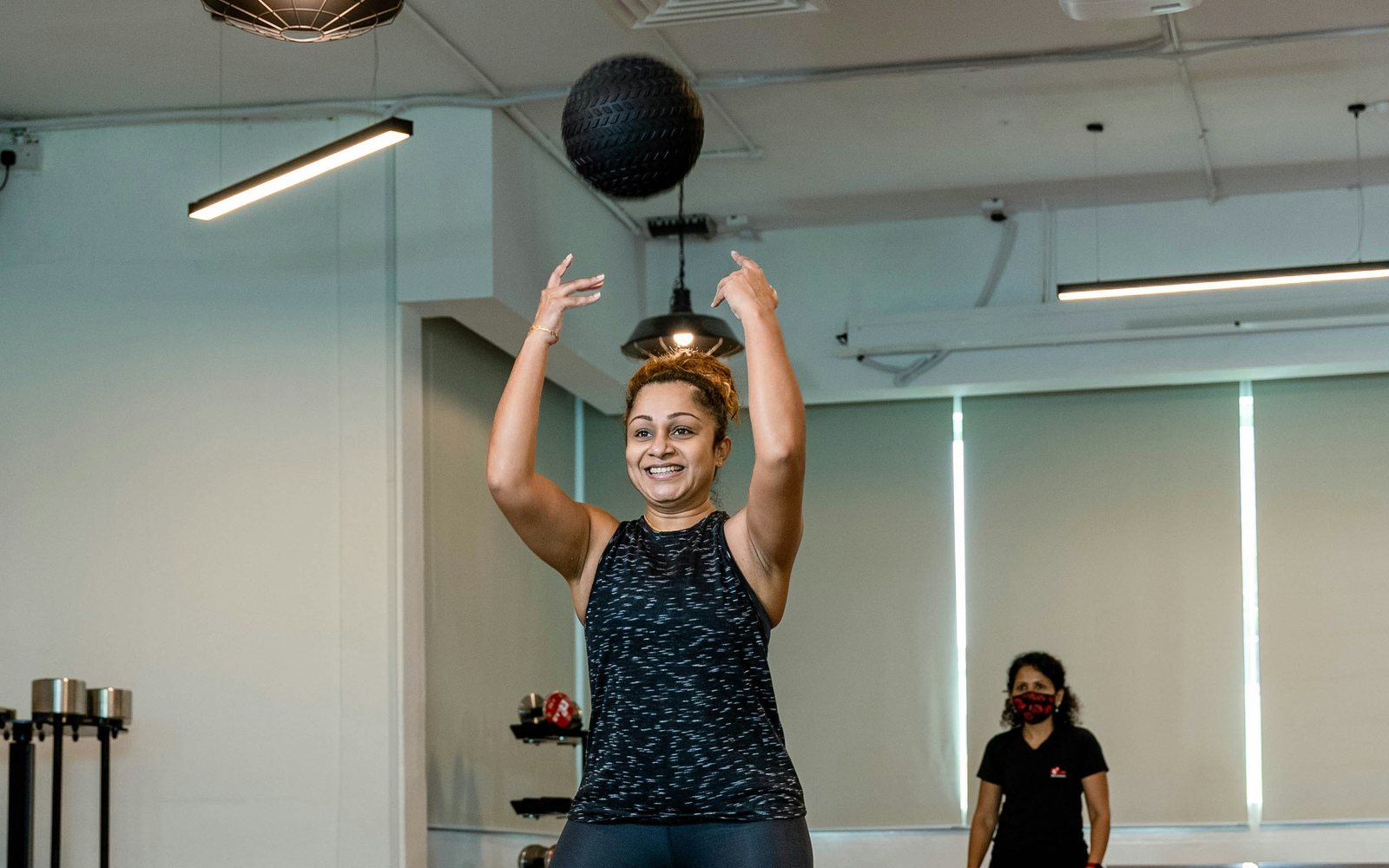 Woman prepares to throw a black medicine ball while an adult observer watches.