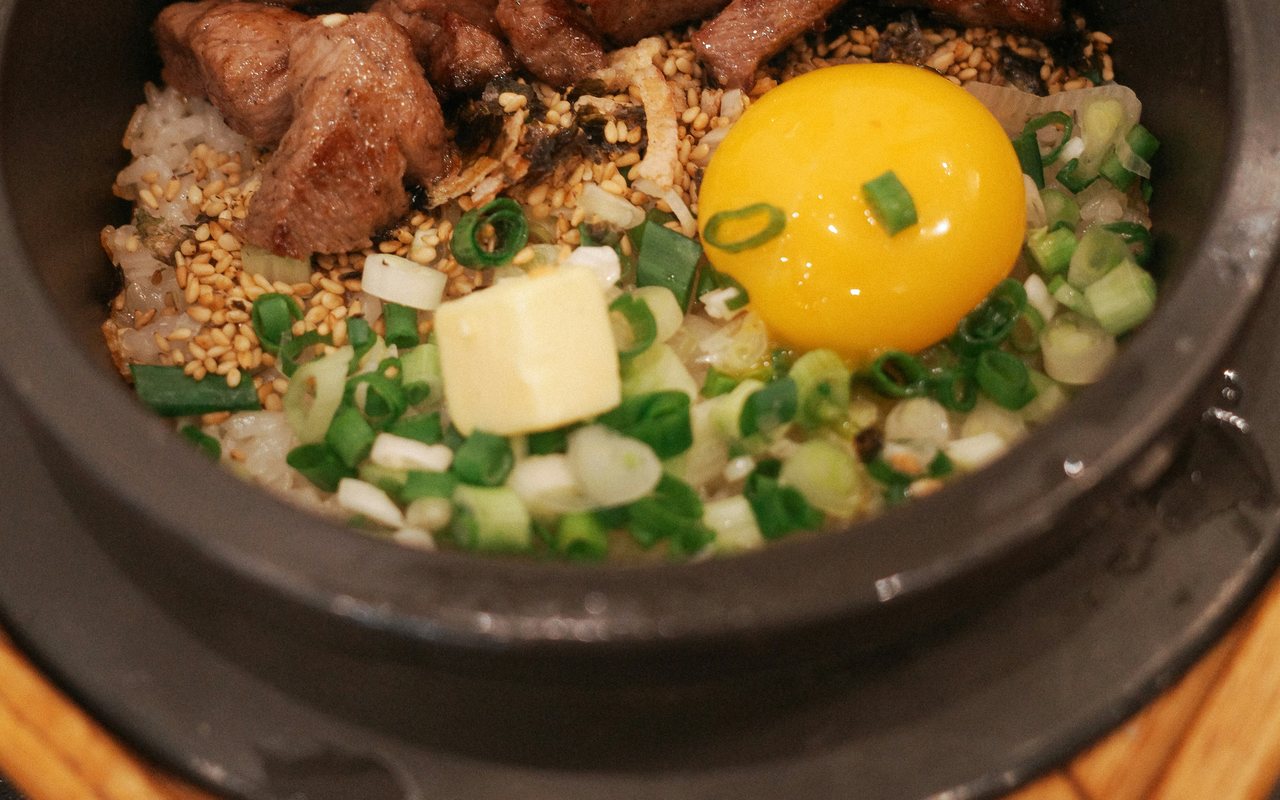 Korean rice bowl with cooked beef, scallions, sesame seeds, seaweed, vegetables, and an egg yolk.