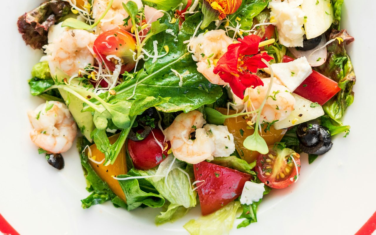 Shrimp salad with leafy greens, carrots, radishes, cucumber, and edible flowers.