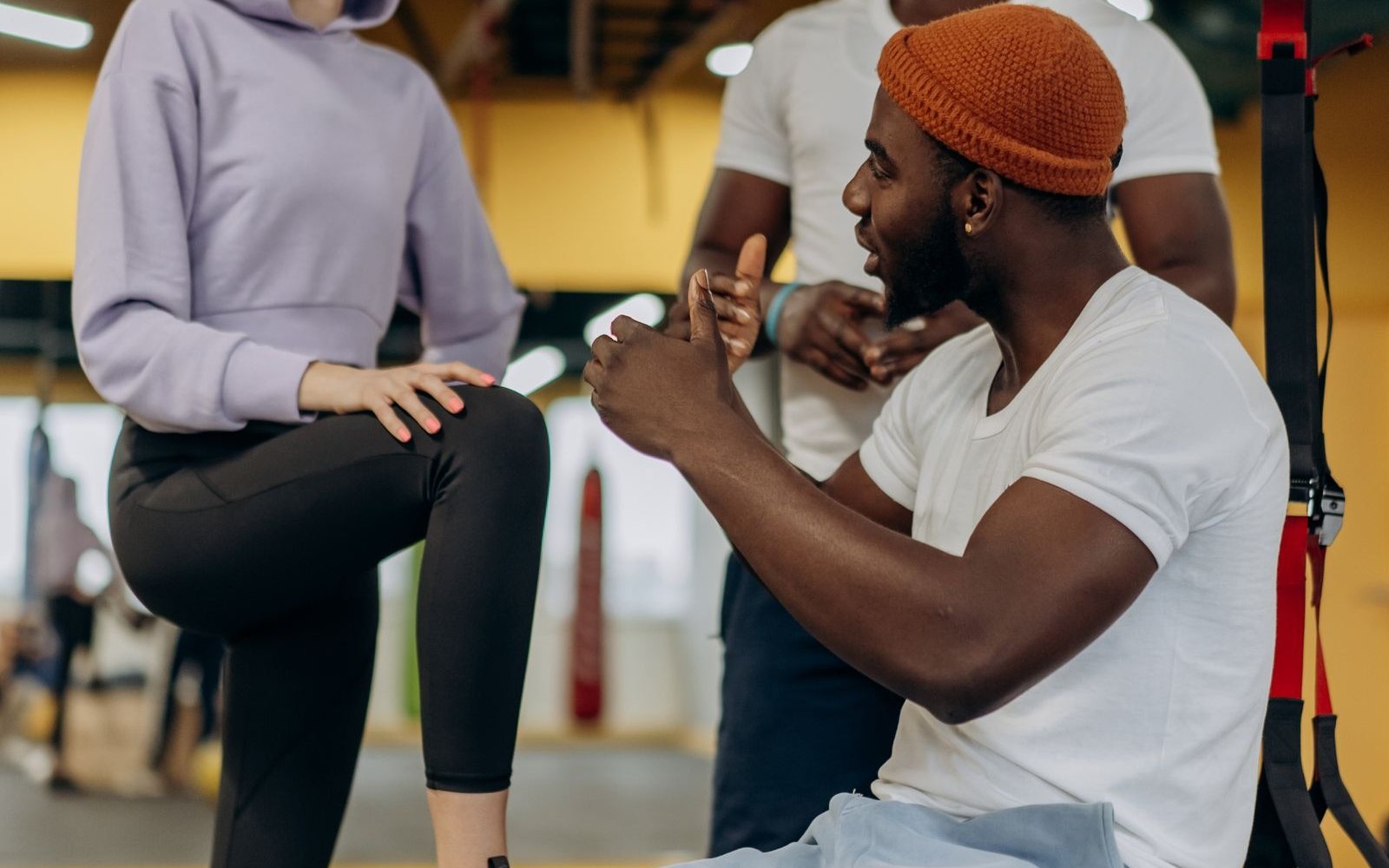 Three adults talk together beside suspension straps in a gym.
