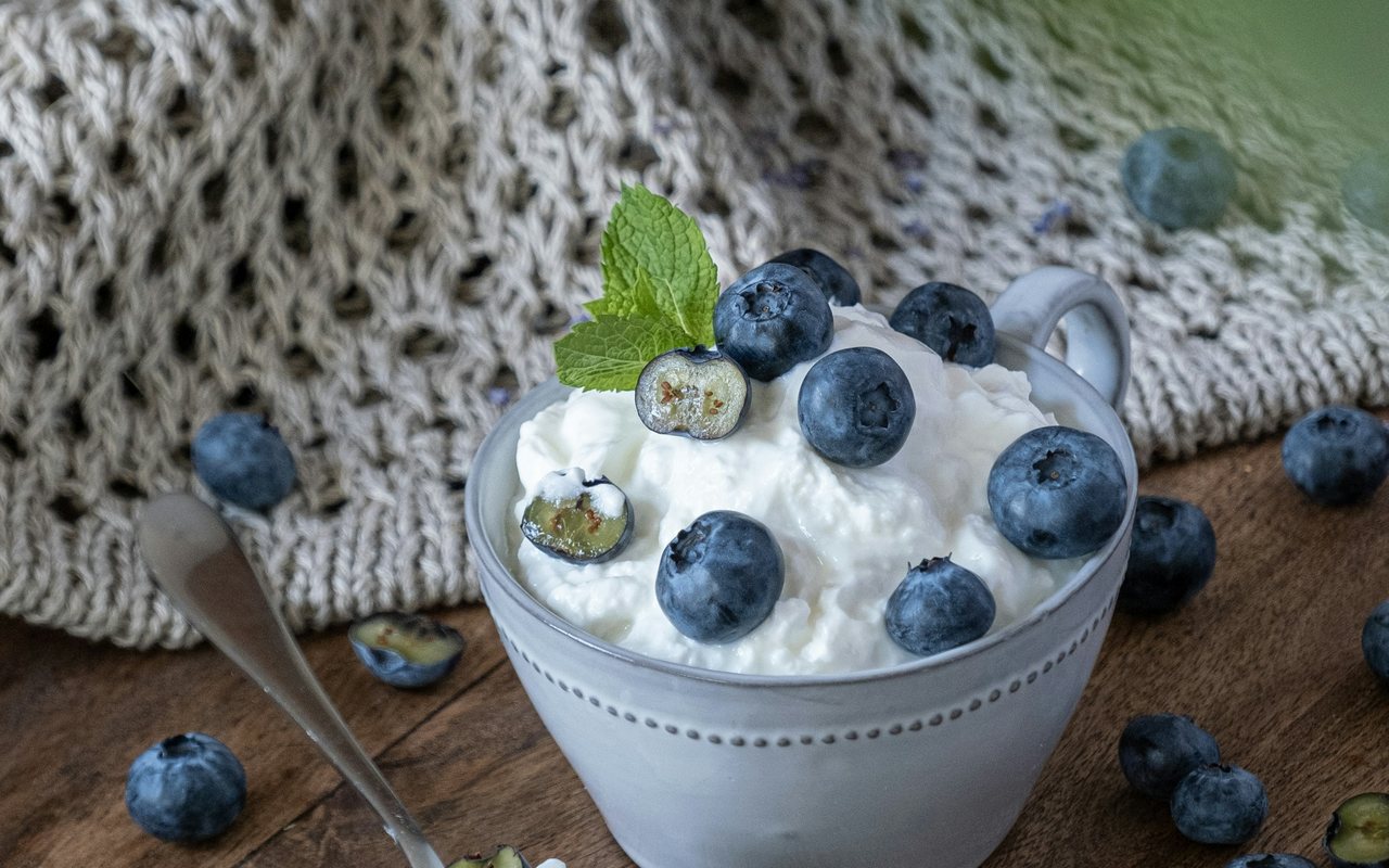 A ceramic cup of cottage cheese topped with blueberries and mint on a rustic table.