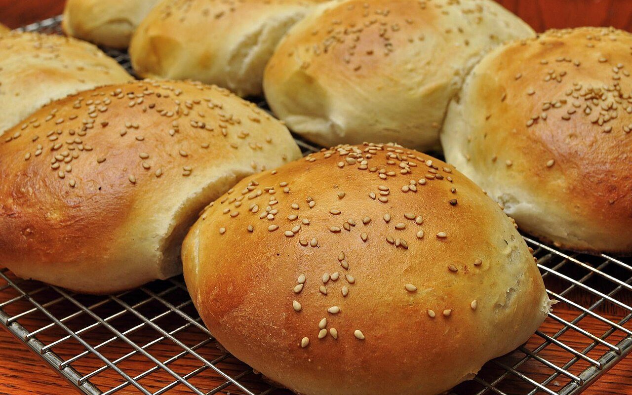 Eight round golden hamburger buns topped with sesame seeds