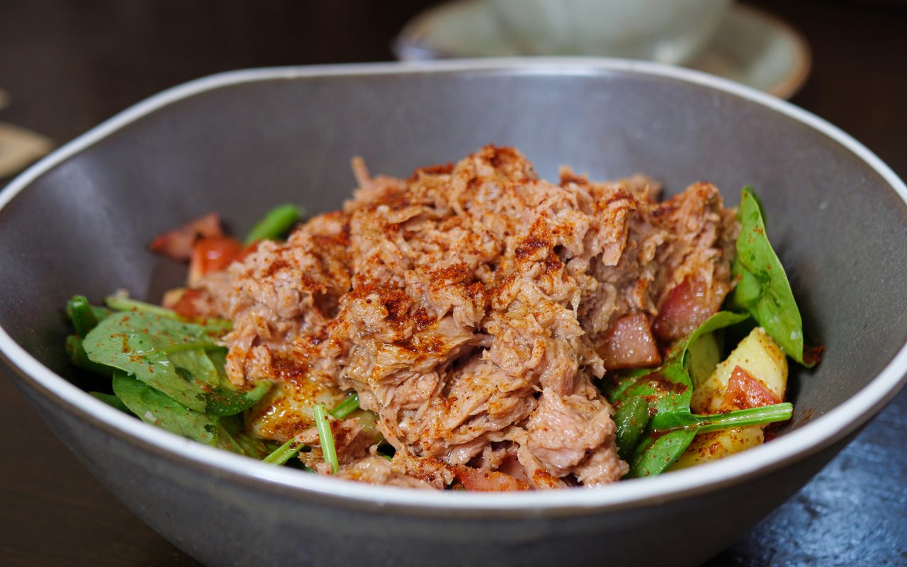 Flaked tuna over spinach, green beans, tomatoes, and red potatoes in a gray bowl.