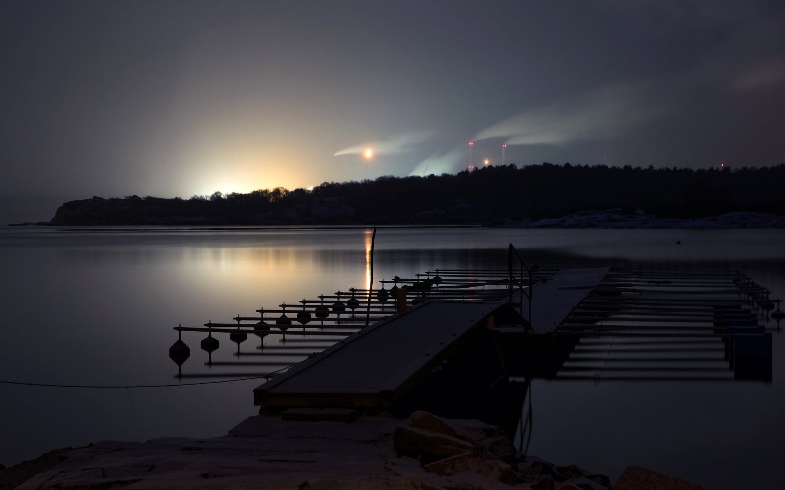 Snowy waterfront and empty docks sit beneath distant industrial lights at night.