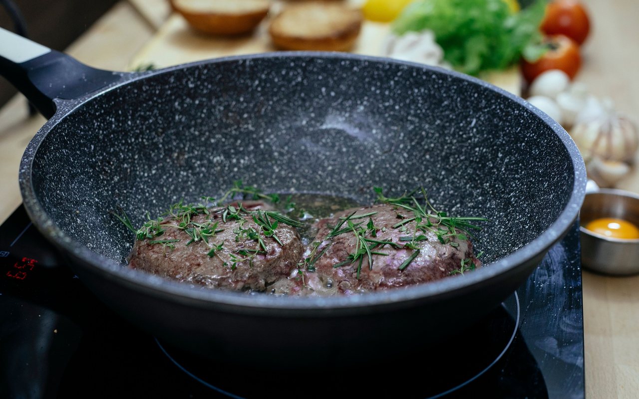 Four browned homemade hamburger patties in a cast-iron skillet