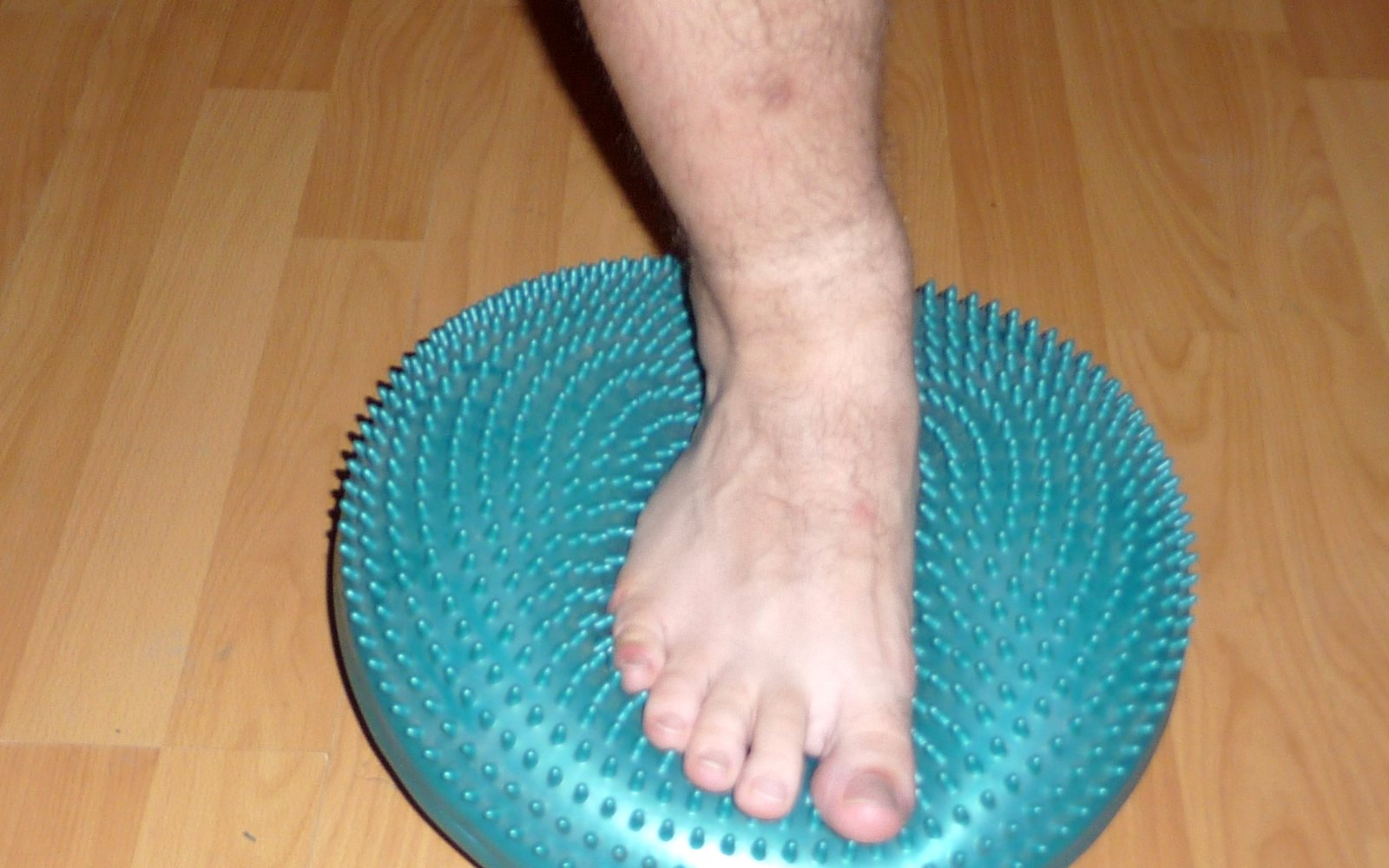 Close-up of a bare foot pressing onto a teal textured balance disc.