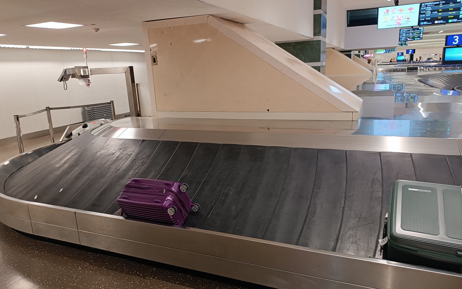 Two suitcases travel around an airport baggage carousel beneath bright terminal lights.