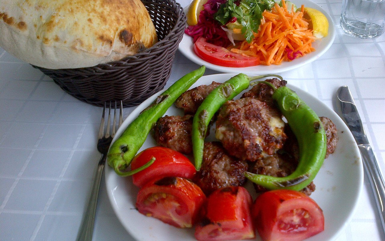 Grilled meat patties with charred green peppers, tomato wedges, bread, and a side salad