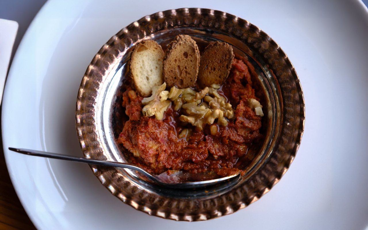 Red muhammara dip in a shallow bowl topped with olive oil and pomegranate molasses