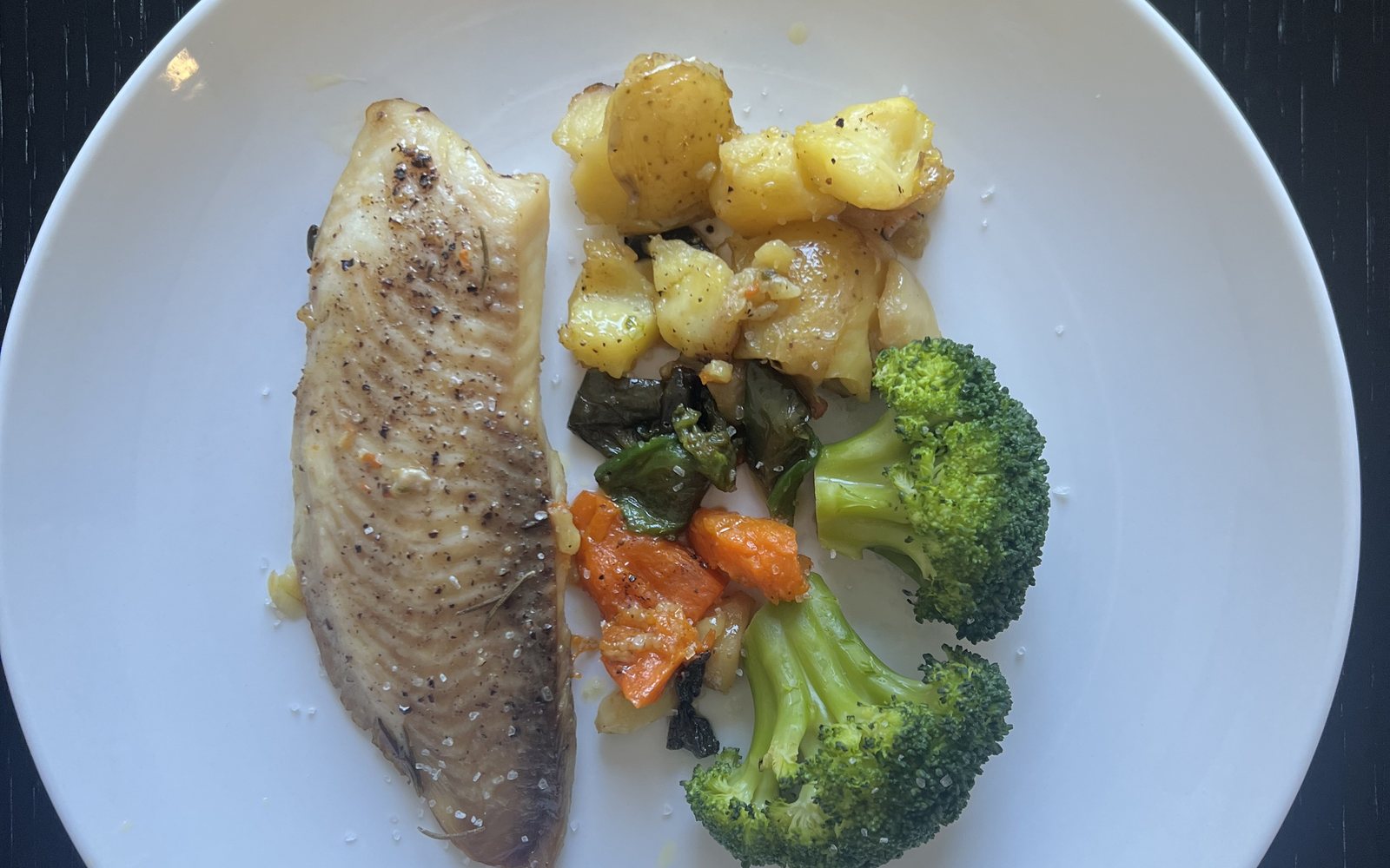 White plate holds a cooked fish fillet, potatoes, broccoli, and other vegetables.