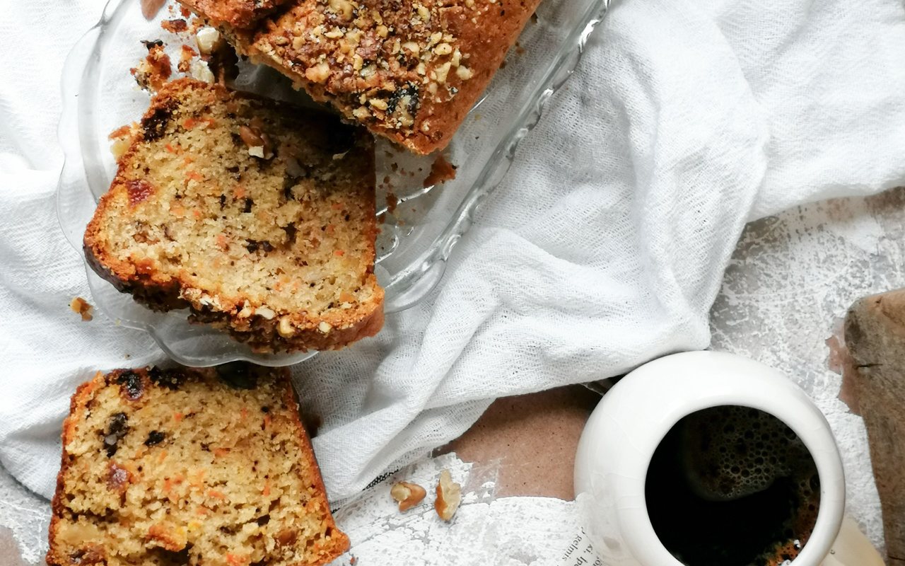 Slices of walnut-topped carrot loaf cake beside a cup of black coffee