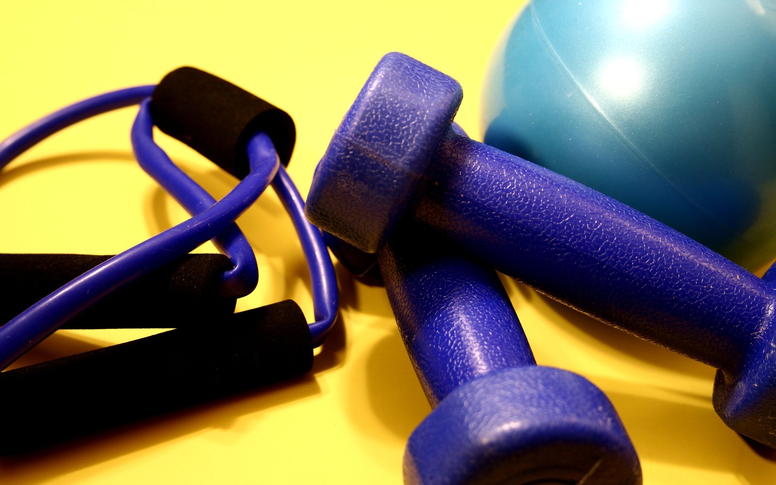 Blue dumbbells, resistance tubes, and an exercise ball arranged on a bright yellow background.