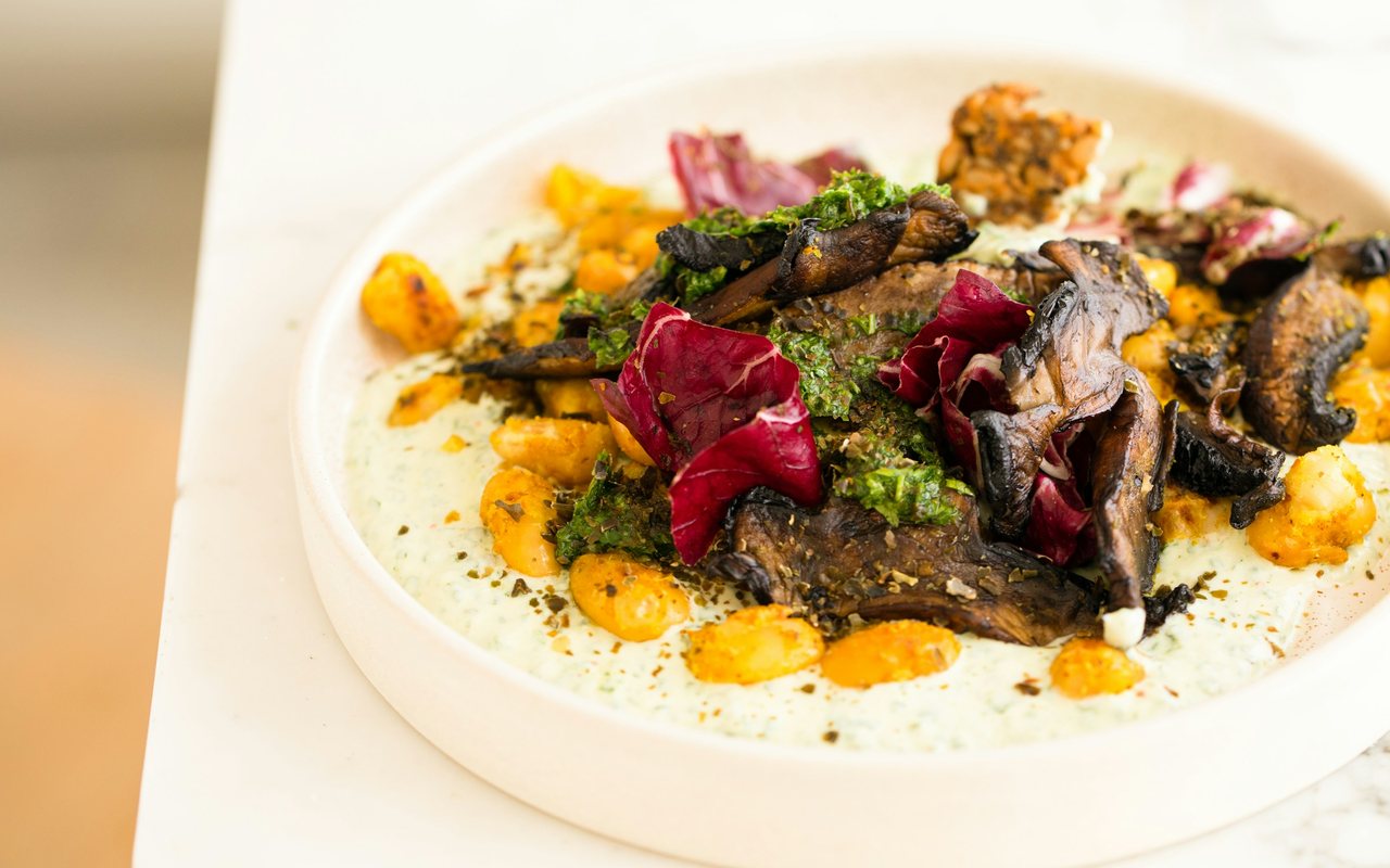 A shallow bowl of butter beans and roasted portobello mushrooms over a pale green sauce, topped with chopped herbs and red leaves.