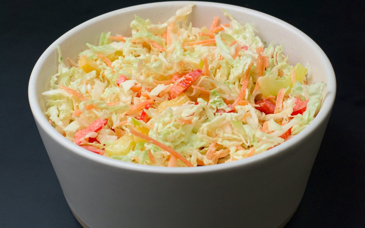 Creamy cabbage and carrot slaw in a white bowl against a dark background.