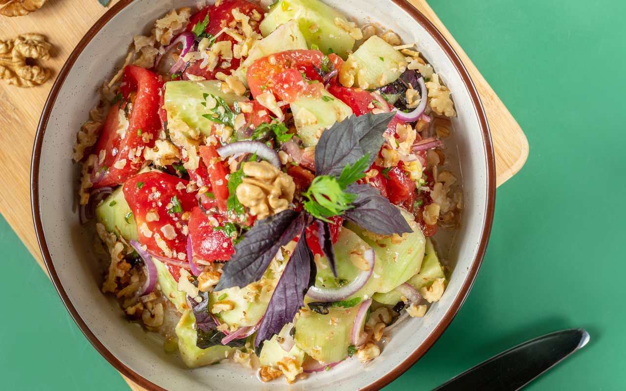 Tomato, cucumber, red onion, fresh herbs, and walnuts in a ceramic bowl