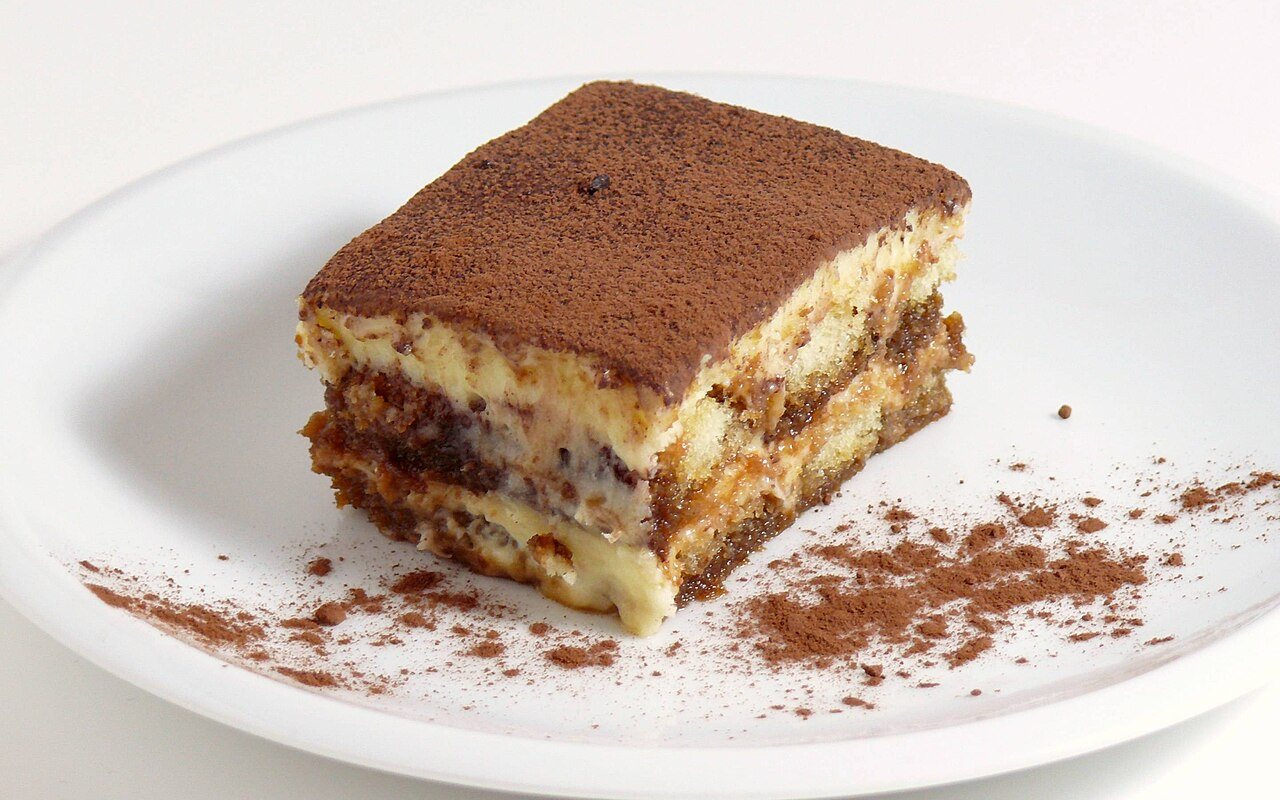 Layered ladyfinger tiramisu covered with cocoa powder in a large glass dish