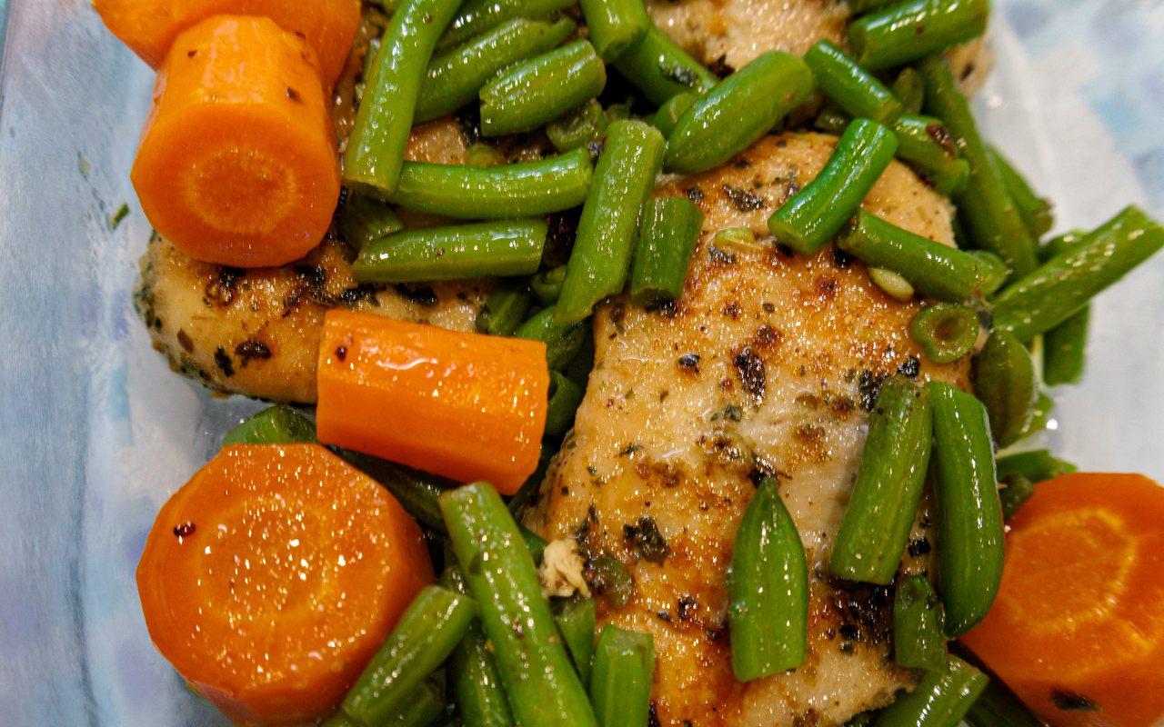 Herb-seasoned chicken breasts with green beans and sliced carrots.