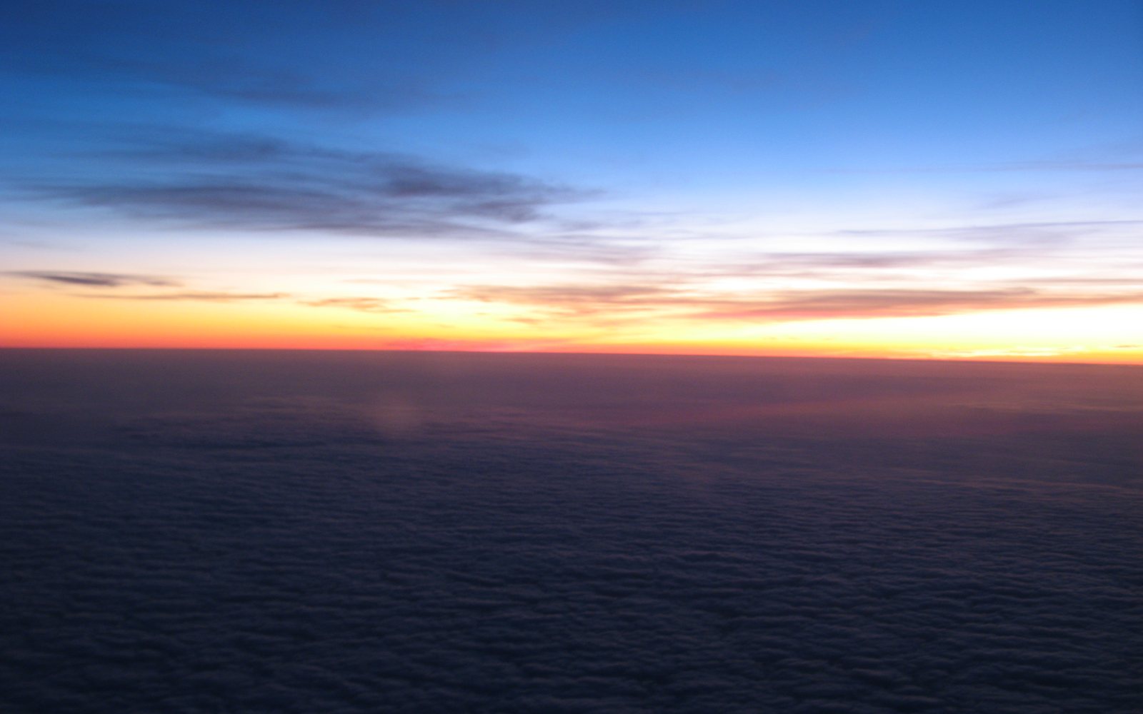 Orange and yellow horizon glows beneath a blue sky above a dark cloud layer.