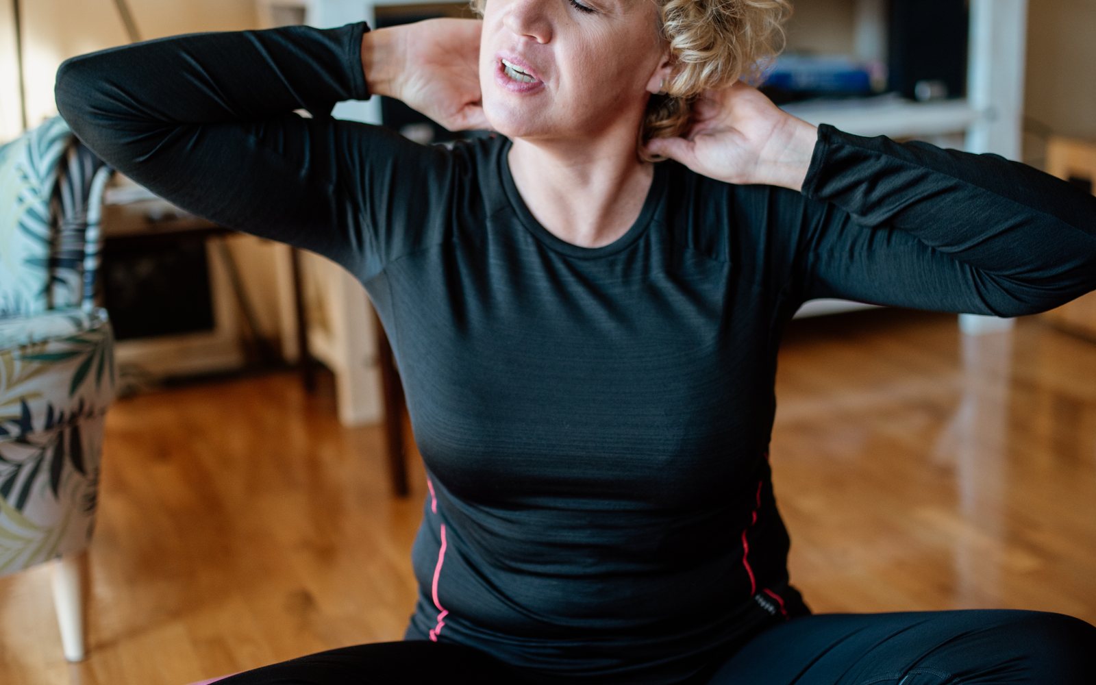 Older woman sits with her eyes closed and both hands resting behind her neck.