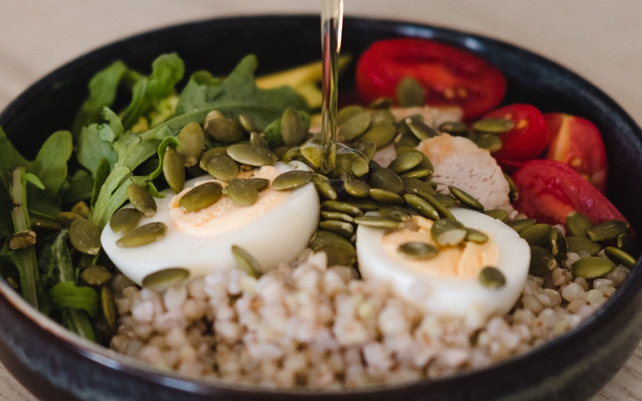 Whole-grain salad with leafy greens, pumpkin seeds, boiled eggs, and cherry tomatoes in a black bowl