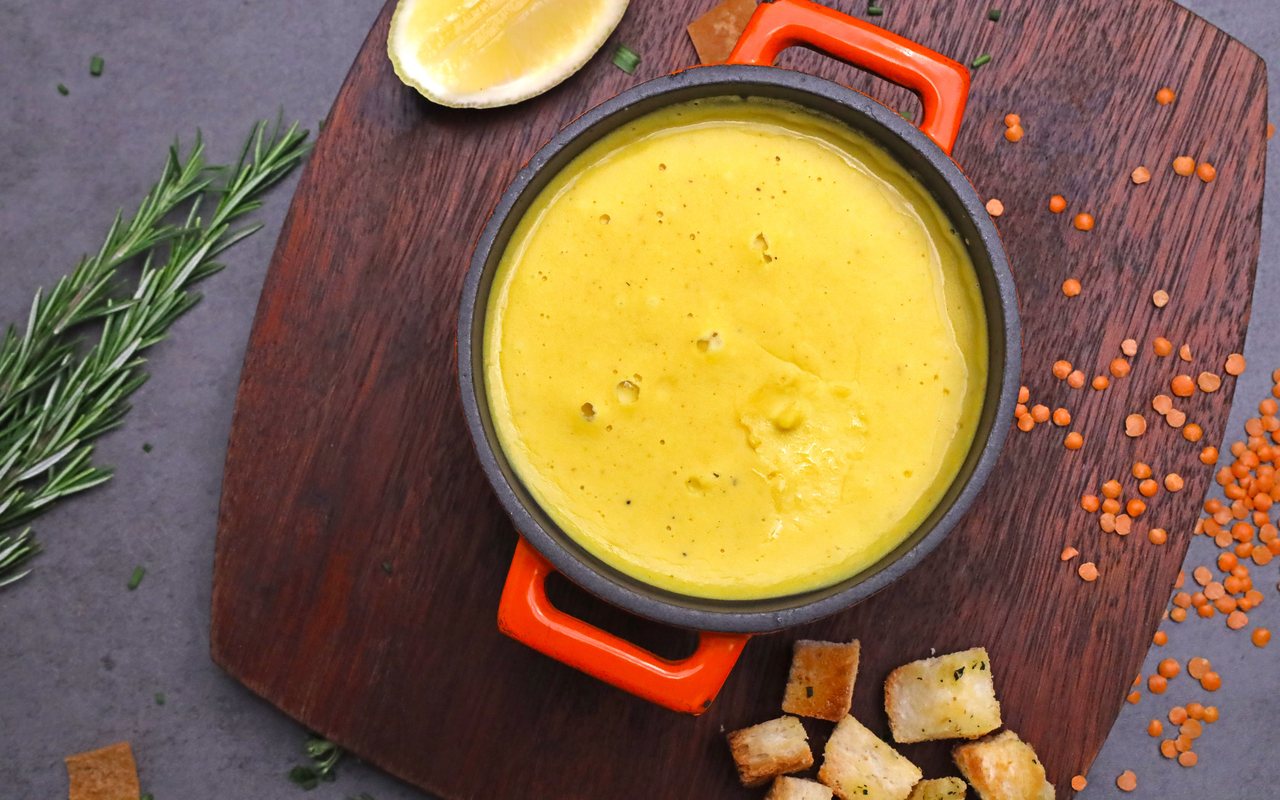 Smooth red lentil soup in a bowl with red pepper oil and a lemon wedge